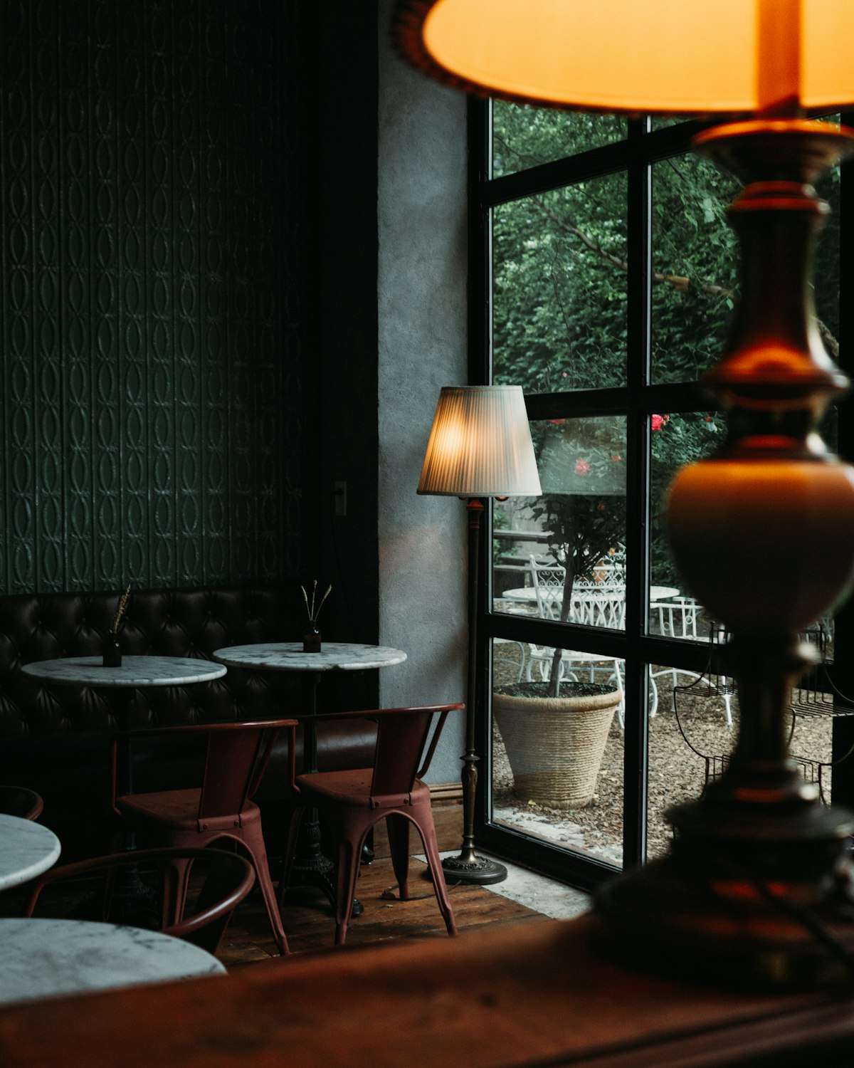 Dining room lit by a brass table lamp beside tall garden windows