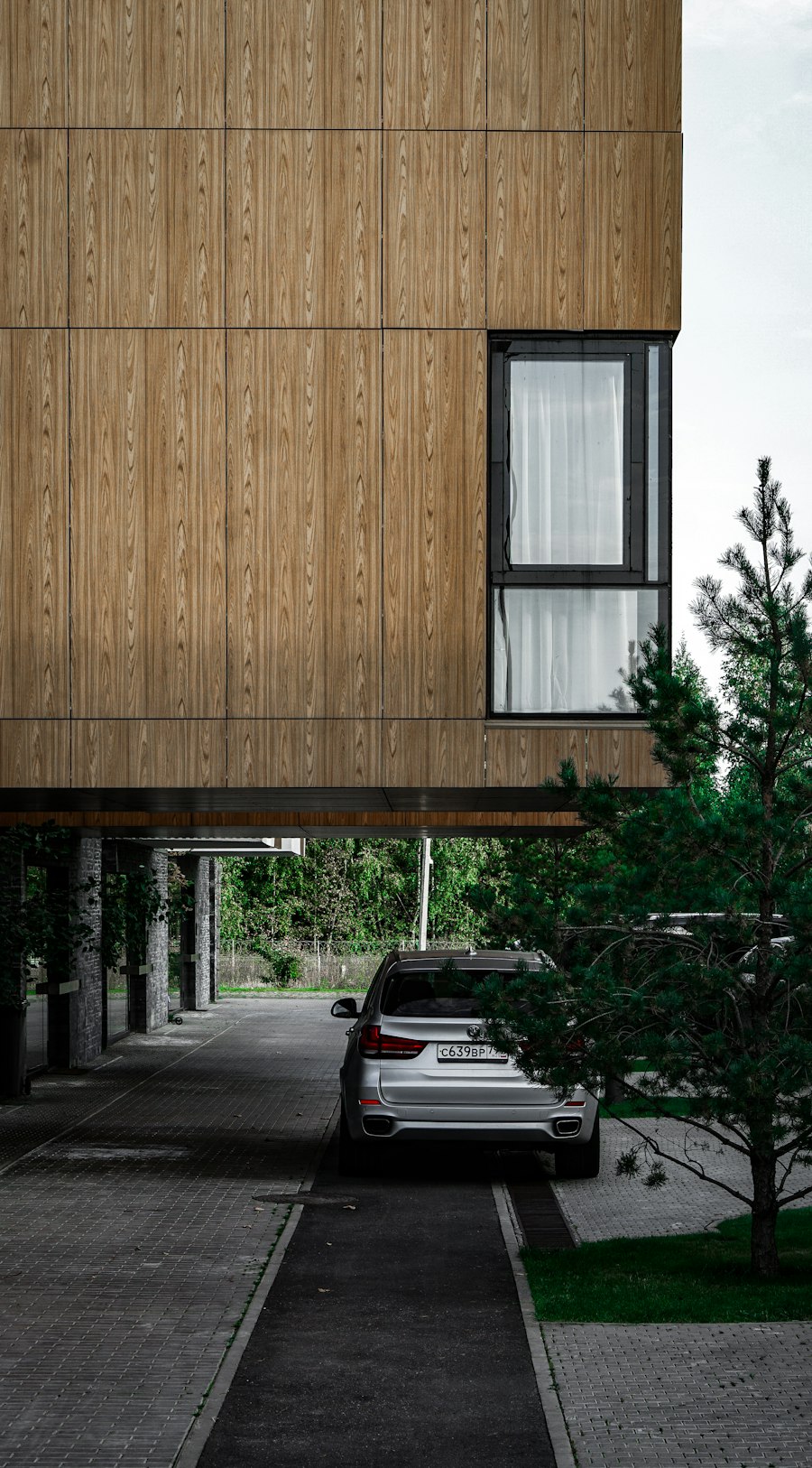 Timber-clad upper floor of a building cantilevered above a driveway