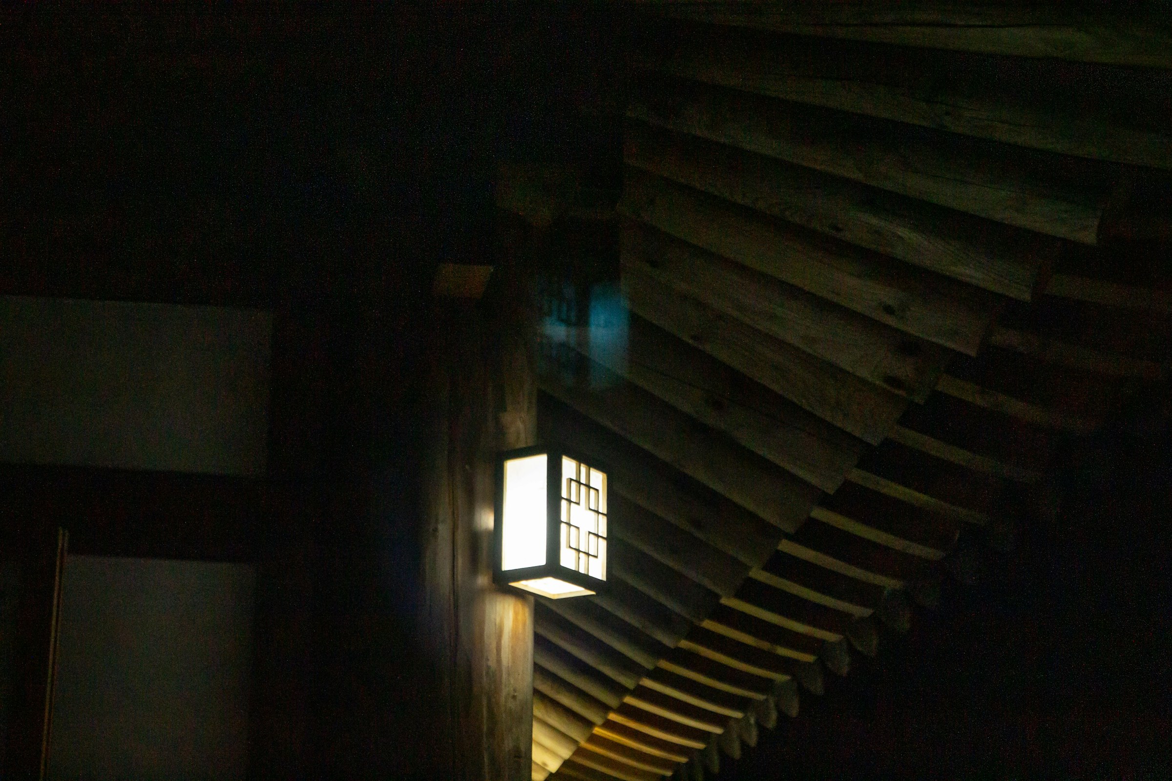 A paper lantern lighting the timber eaves of a house entrance at night